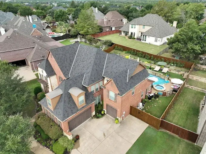 An aerial view of a house with a brown roof and a pool in the backyard.