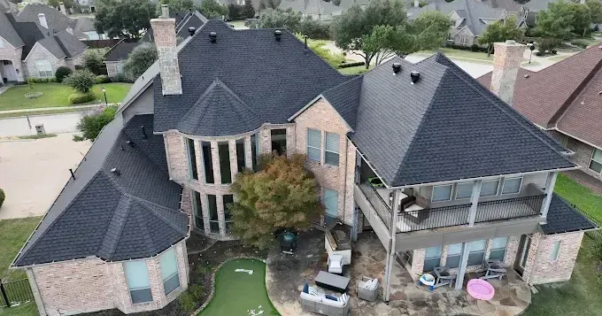 Aerial view of a large two-story brick house with dark roof, landscaped yard, and covered patio.