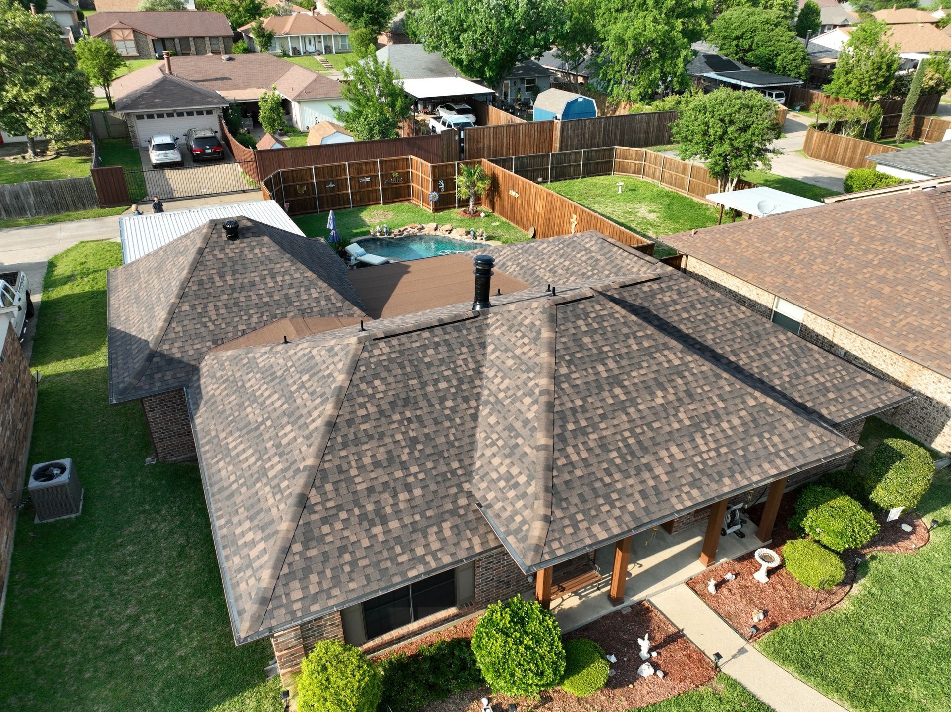 An aerial view of a house with a brown roof and a pool in the backyard.