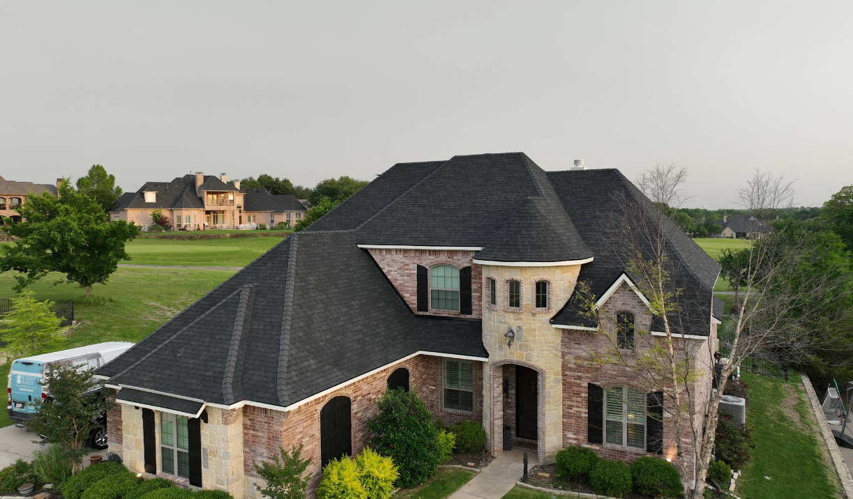 Large brick house with dark roof and landscaped yard in a suburban neighborhood