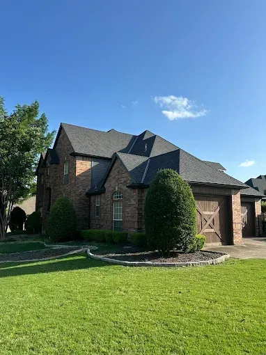 A large brick house with a gray roof and a large lawn in front of it.
