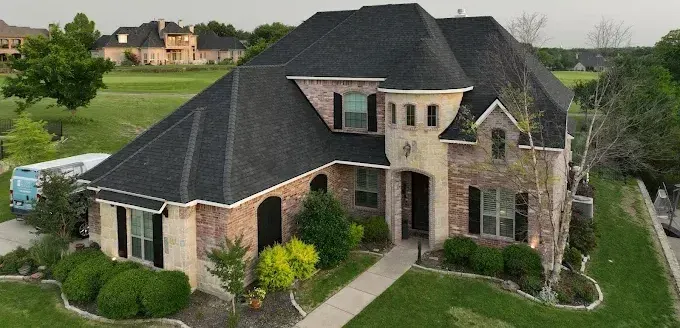 Large brick suburban house with a dark roof, landscaped yard, and driveway
