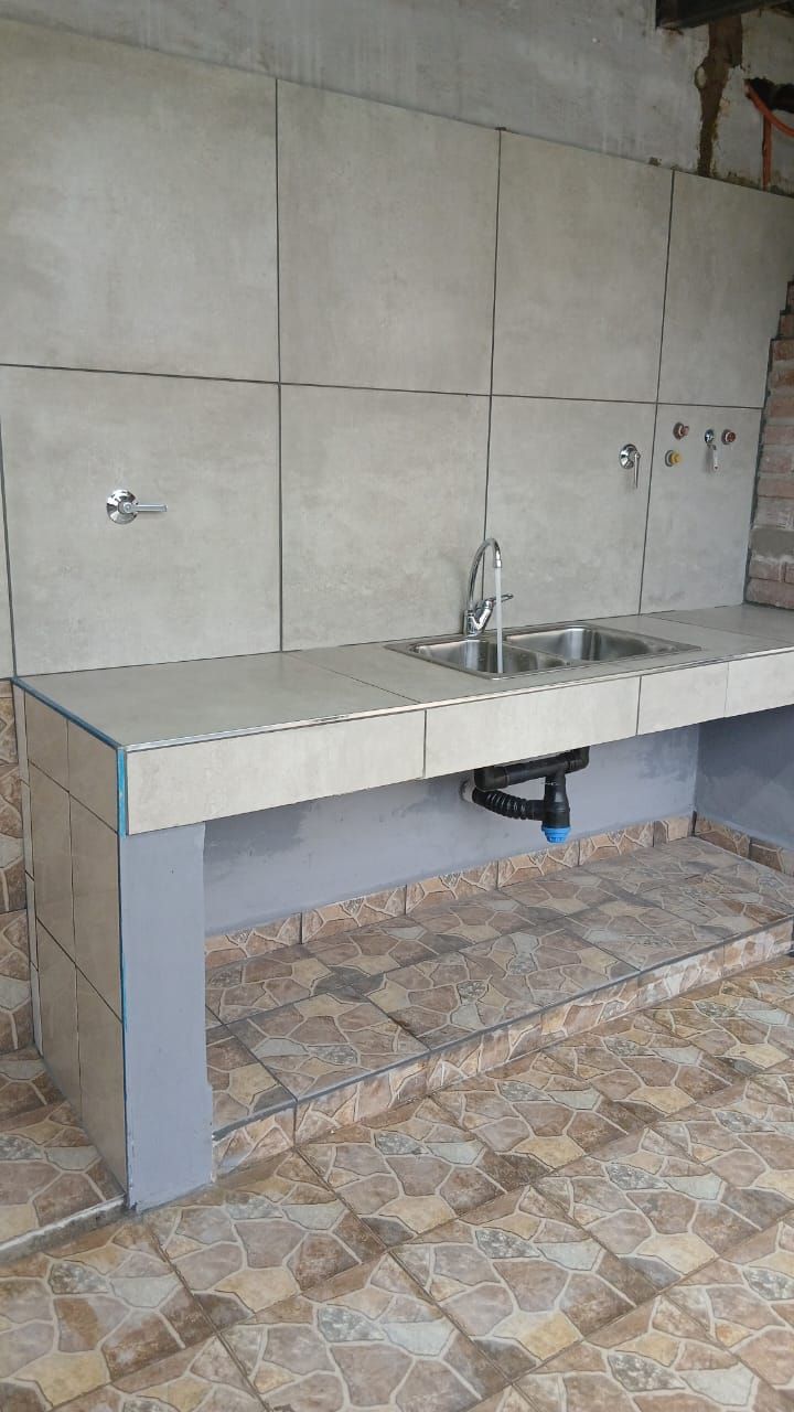 Encimera de fregadero exterior de hormigón con grifo contra una pared de azulejos y suelo estampado.