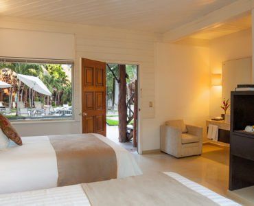 Hotel room with two beds, an open door, and a view of a patio with umbrellas and trees.