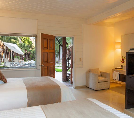 Hotel room with two beds, an open door to a garden, and a window overlooking a patio.