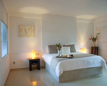 Bright hotel room with a white bed, neutral tones, and warm lighting.