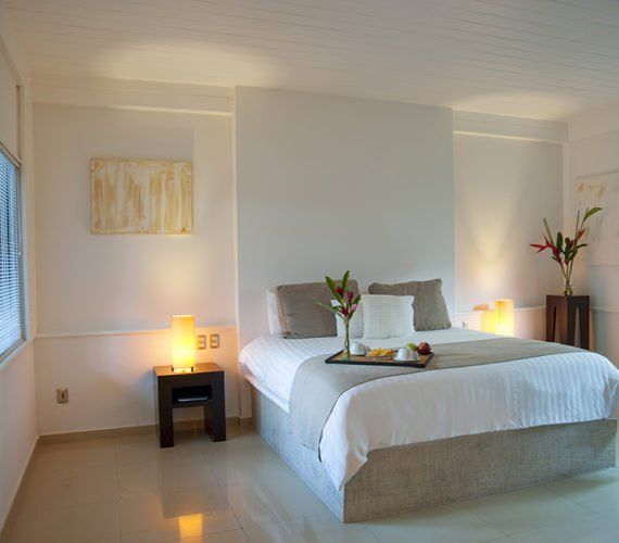 Bedroom with a large bed, tray of food, and two bedside lamps. White walls and tan flooring.