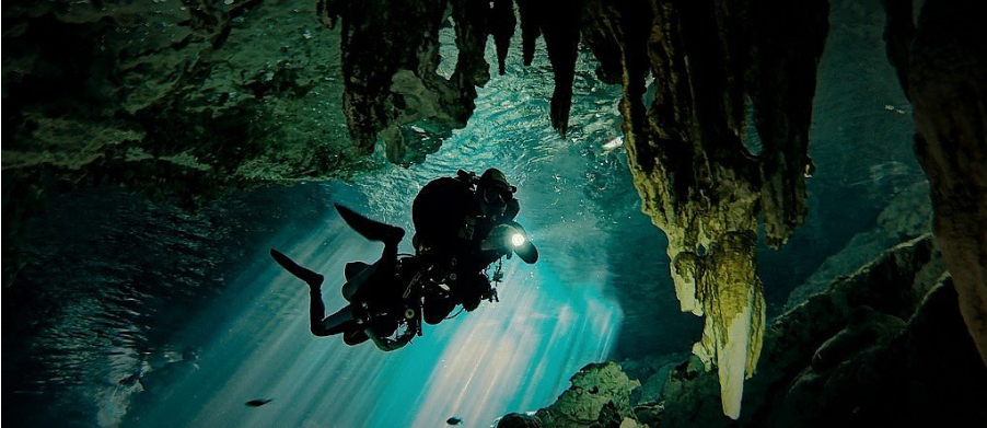 Buzos explorando una cueva submarina; estalactitas y agua turquesa.