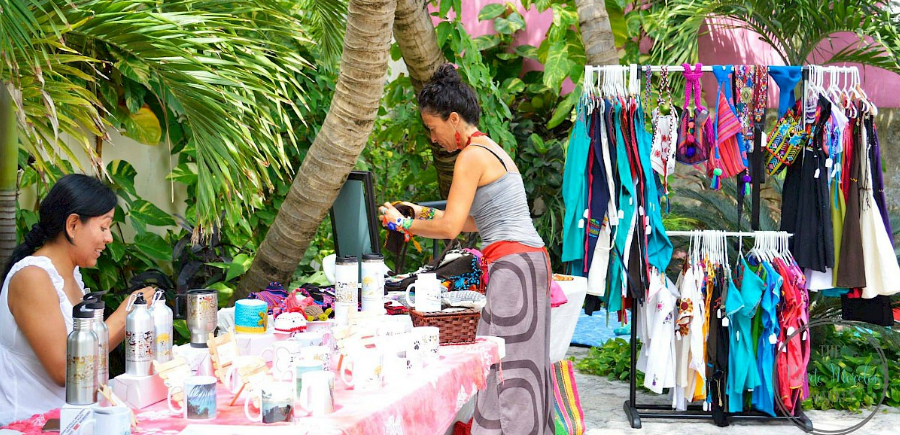 Dos mujeres en un mercado de ropa y joyería al aire libre; percheros con ropa colorida en exhibición.