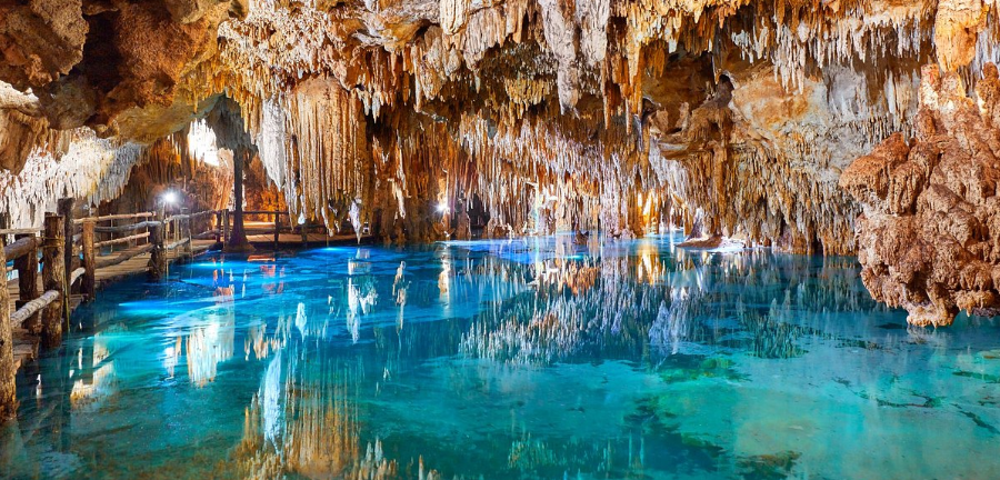 Cueva con agua turquesa, pasarela de madera y numerosas estalactitas.