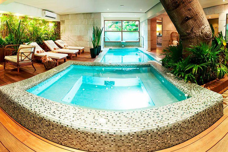 Indoor spa with pools, lounge chairs, and tropical plants.