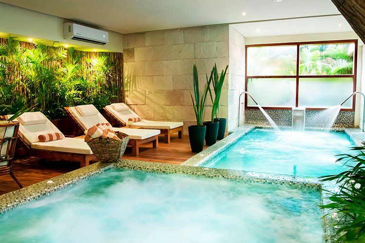 Spa with chaise lounges, hot tub, and pool with waterfalls; lush greenery and stone walls.