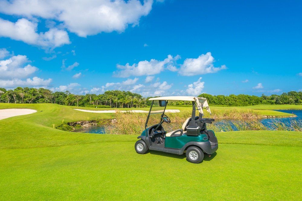 Green golf cart on a vibrant green fairway with a blue sky, near a lake.