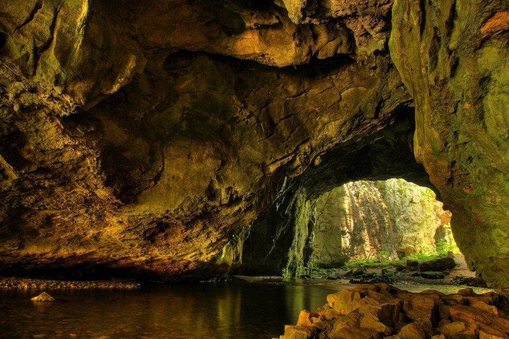 A cave interior with a water-filled foreground and arched opening leading to sunlight.