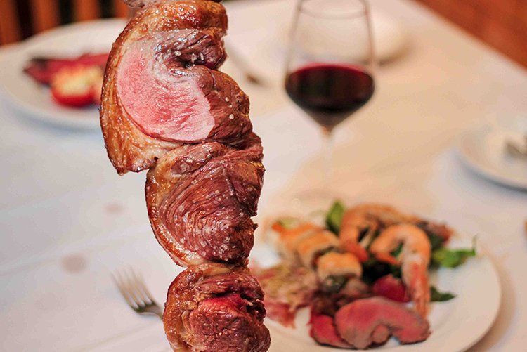 Skewered grilled meat, steak, presented at a table setting, with a glass of red wine in the background.