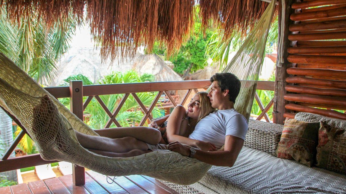 Couple relaxing in a hammock on a balcony, surrounded by lush vegetation and rustic wood.