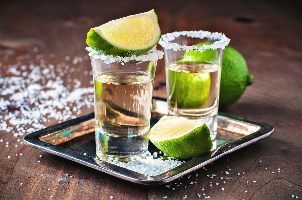 Two tequila shots with salt rims, lime wedges, and a lime on a tray.