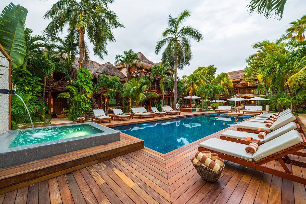 Pool and hot tub at a tropical resort, wooden deck with lounge chairs, palm trees.