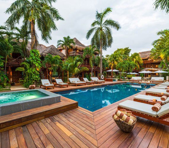 Swimming pool area with wooden deck, lounge chairs, and palm trees.
