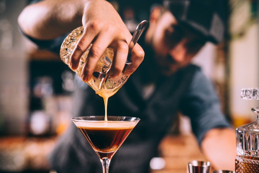 Camarero sirviendo una bebida en una copa de martini, creando un cóctel en capas.