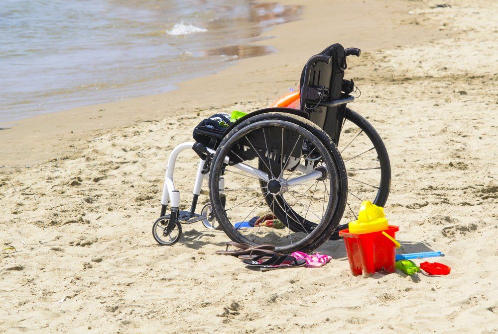 Wheelchair on sandy beach near the water with beach toys.