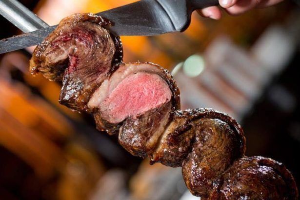 Grilled beef on a skewer, being sliced with a knife; reddish-pink interior, flames visible.