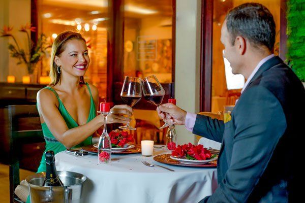 Pareja brindando con vino en una cena romántica. La mujer sonríe con un vestido verde. El hombre lleva blazer. Restaurante.
