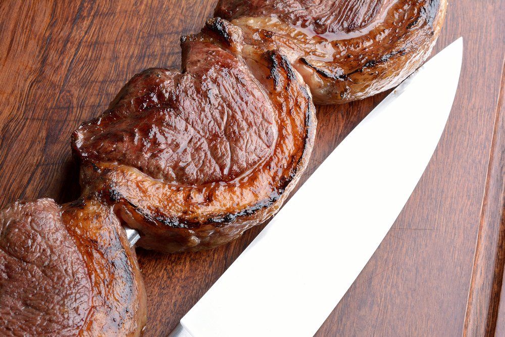 Grilled beef steaks on a wooden board with a silver knife.