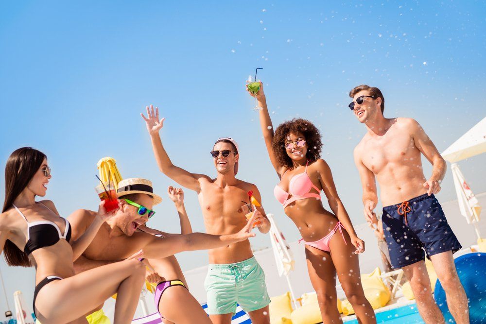 People dancing and celebrating by a pool on a sunny day.