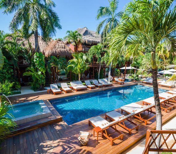 Swimming pool surrounded by palm trees, lounge chairs, and tropical buildings.
