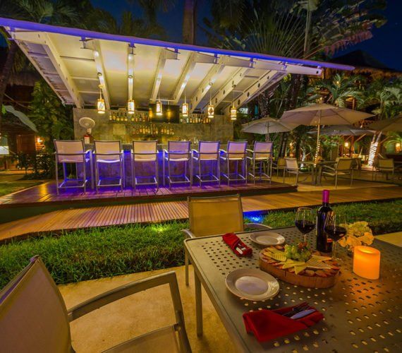 Outdoor bar with illuminated barstools and a table set for dinner; night setting.