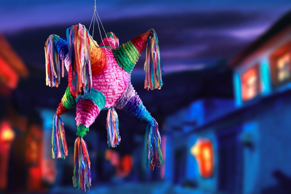 Colorful star-shaped piñata hanging in front of a blurred background of buildings with warm light.