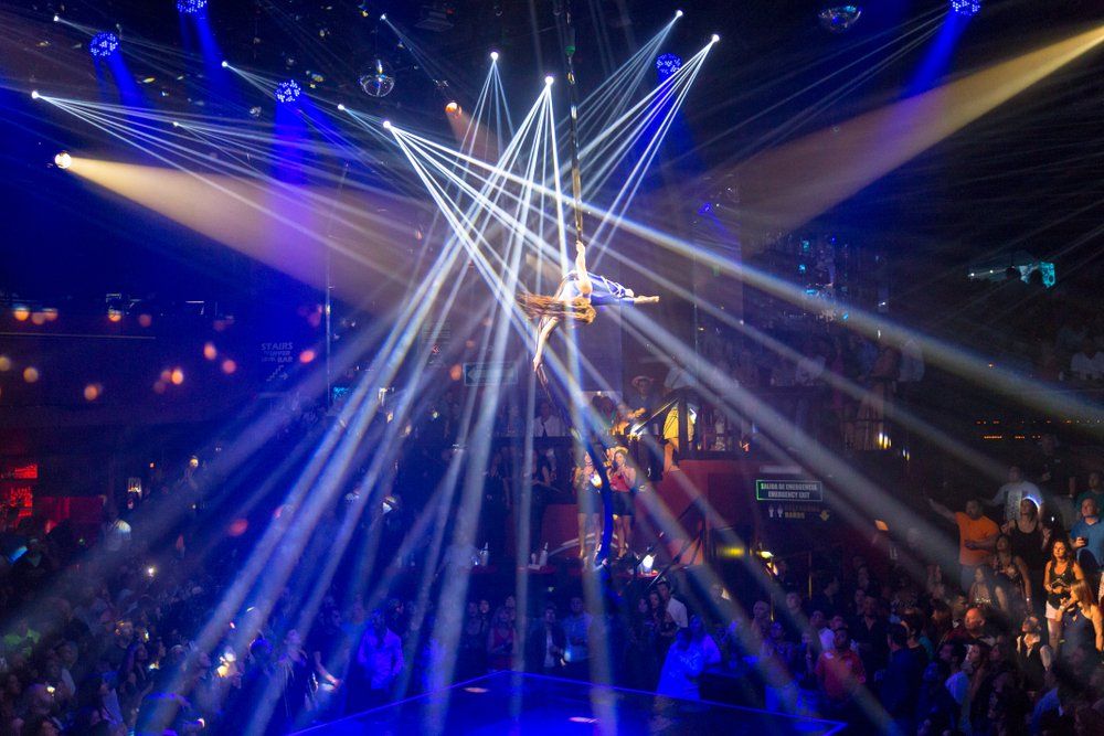Aerial performer suspended, illuminated by blue and white stage lights; crowd below.