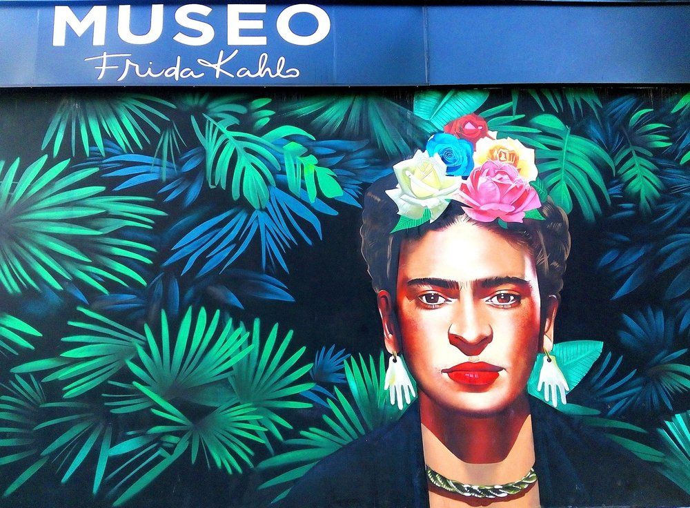 Mural of Frida Kahlo with floral crown against a backdrop of green tropical leaves;