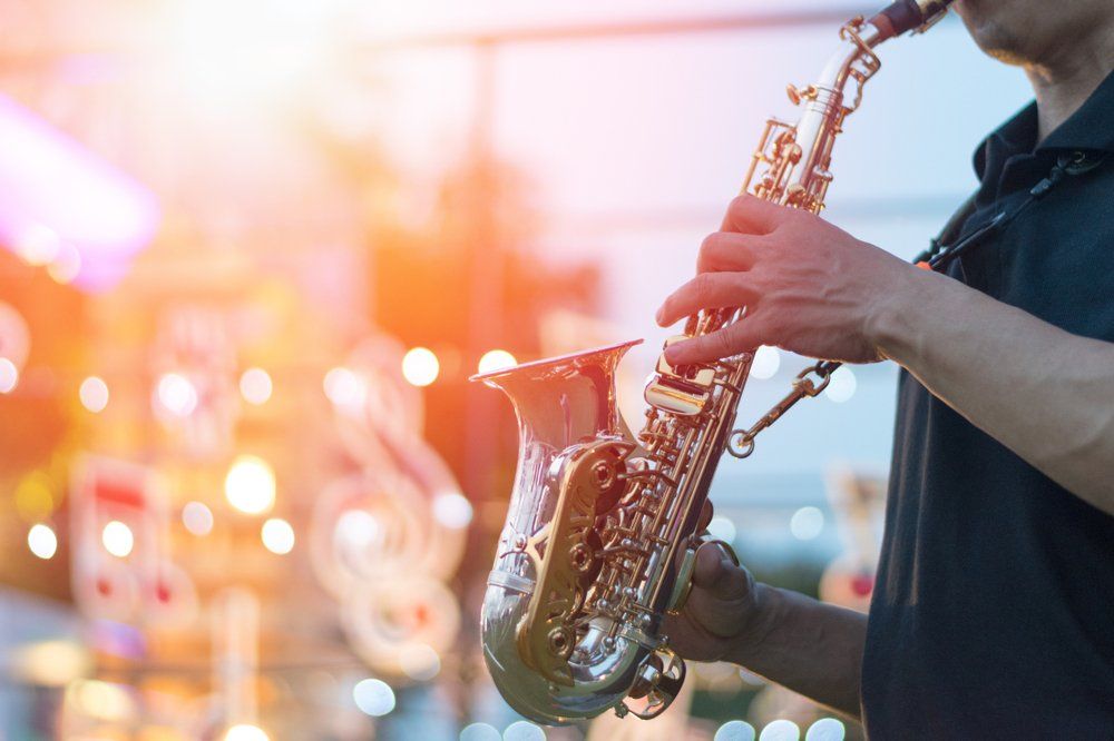 Saxophone player performing outdoors with blurred lights in the background.