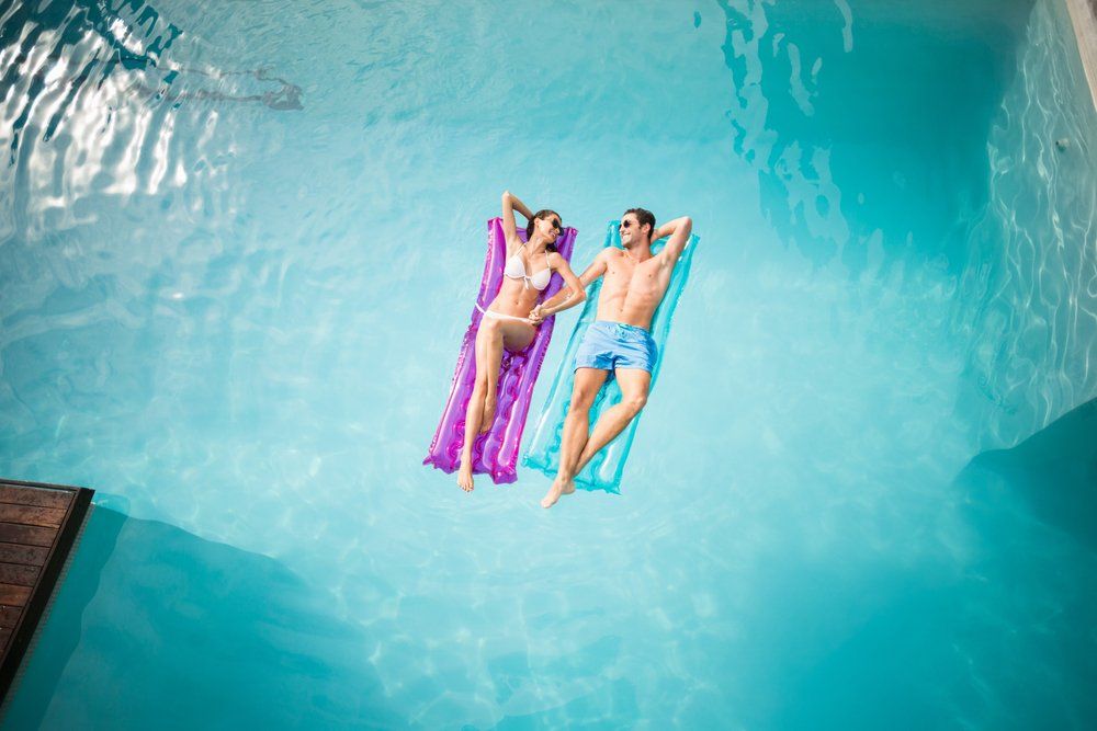 Couple relaxing on inflatable rafts in a turquoise pool.