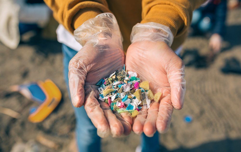 Person holding handful of colorful plastic pieces, wearing gloves, on a beach.