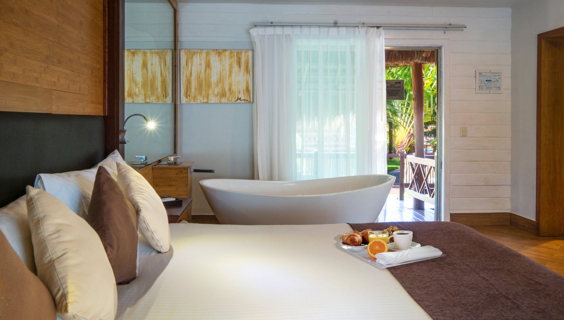 Bedroom with bed, bathtub, and open doors to patio; breakfast tray visible.