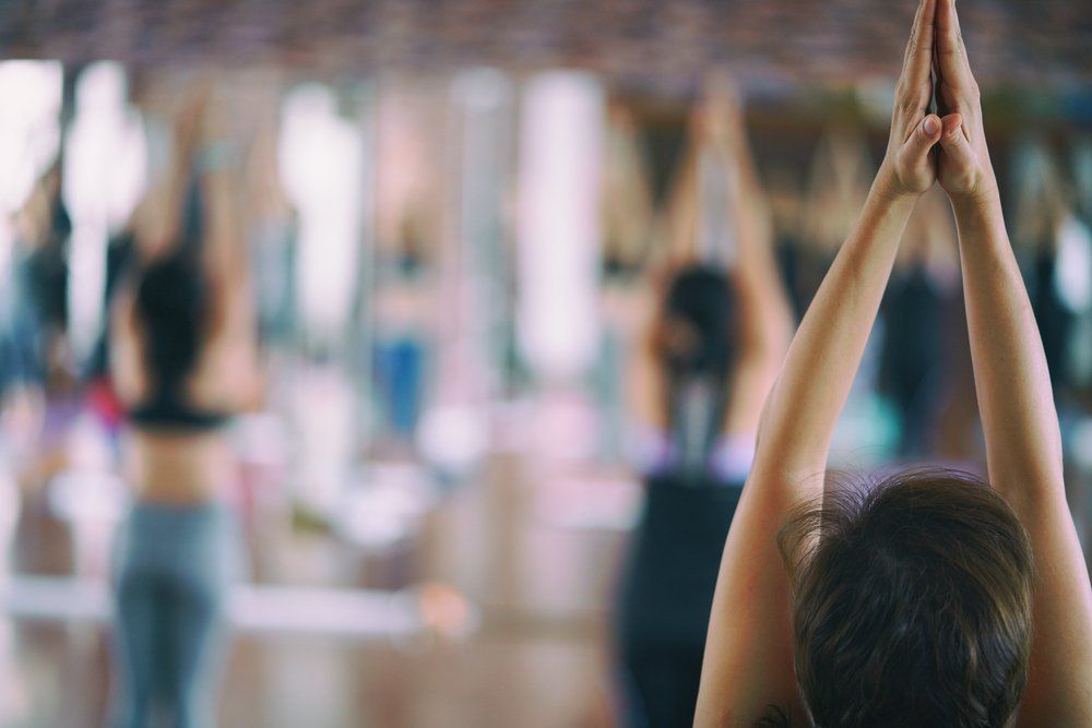 Personas en una clase de yoga, con los brazos levantados por encima de la cabeza y las palmas juntas.