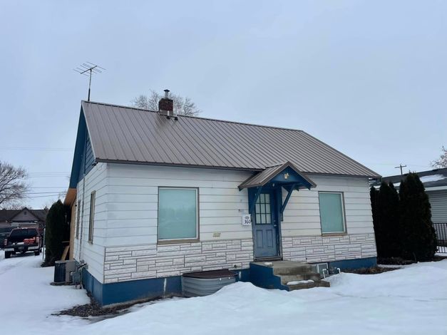 Small white house with blue trim and a snow-covered yard in winter