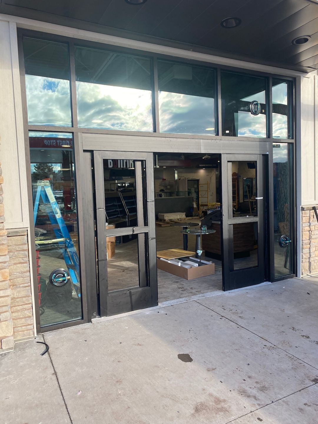 Storefront entrance with sliding glass doors and open doorway; ladder visible inside under an awning
