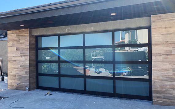Modern building exterior with large glass garage door and stone siding reflected in the panels