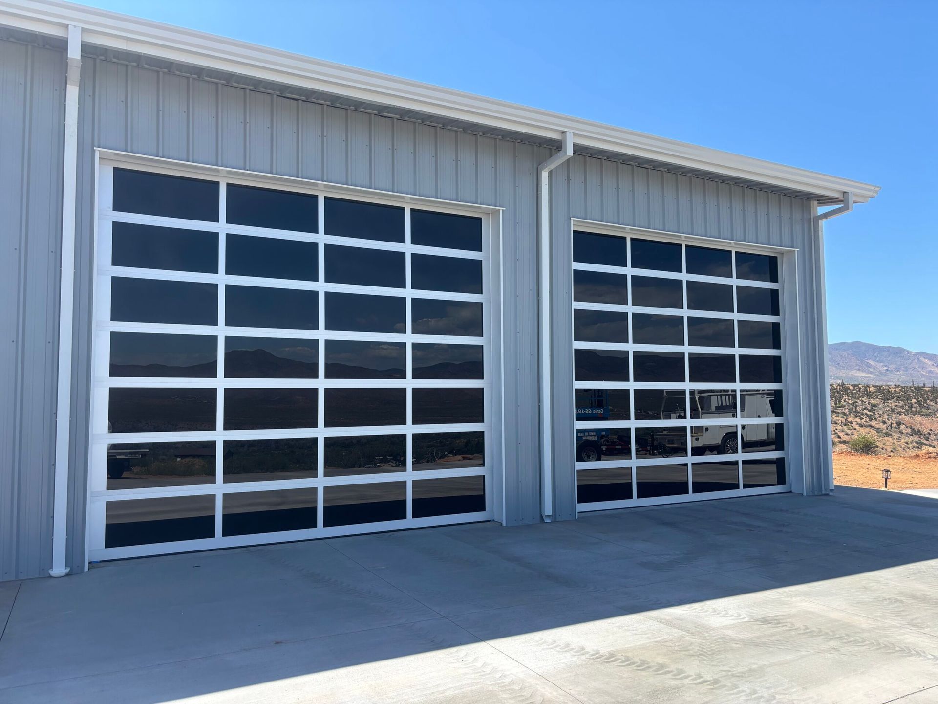 Two gray metal garage doors on a light blue industrial building in a desert setting
