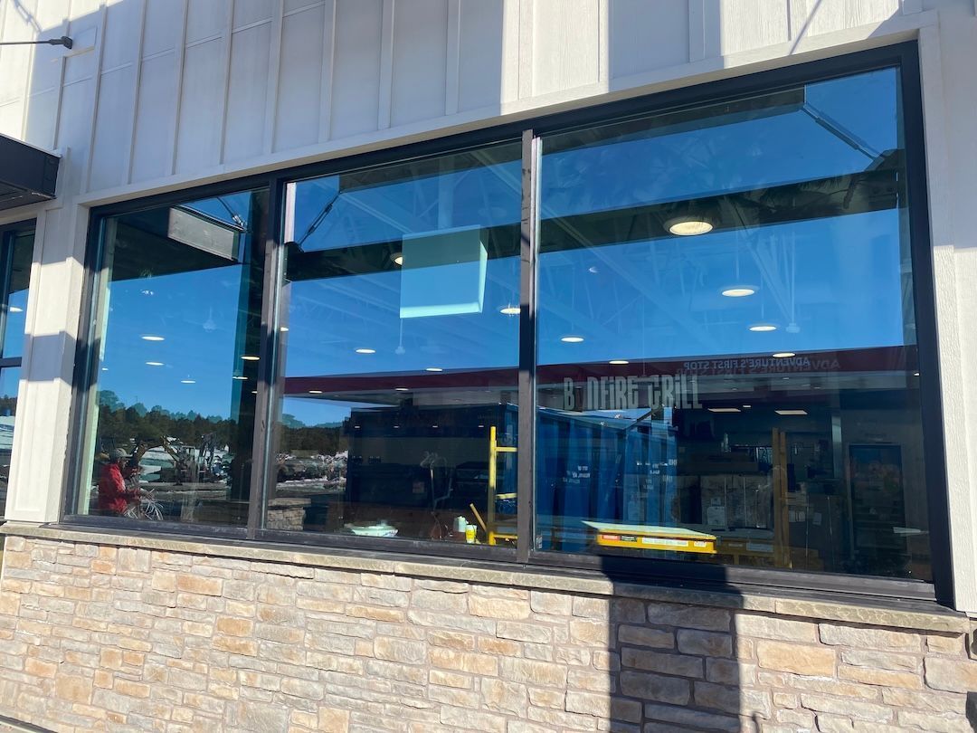 Storefront with large reflective windows and stone facade under a blue sky