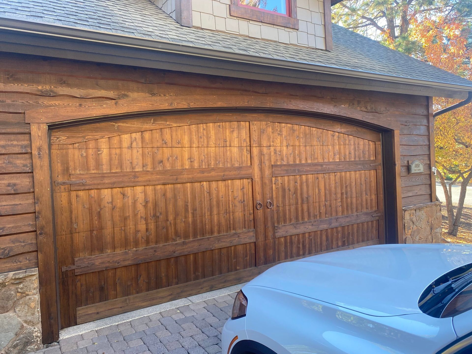 Wooden double garage doors on a brick house, with a silver car parked in front.