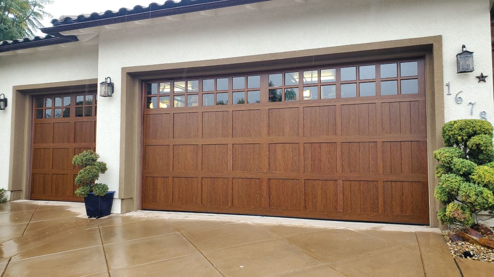 Modern house exterior with a large wooden garage door, potted plants, and a wet driveway