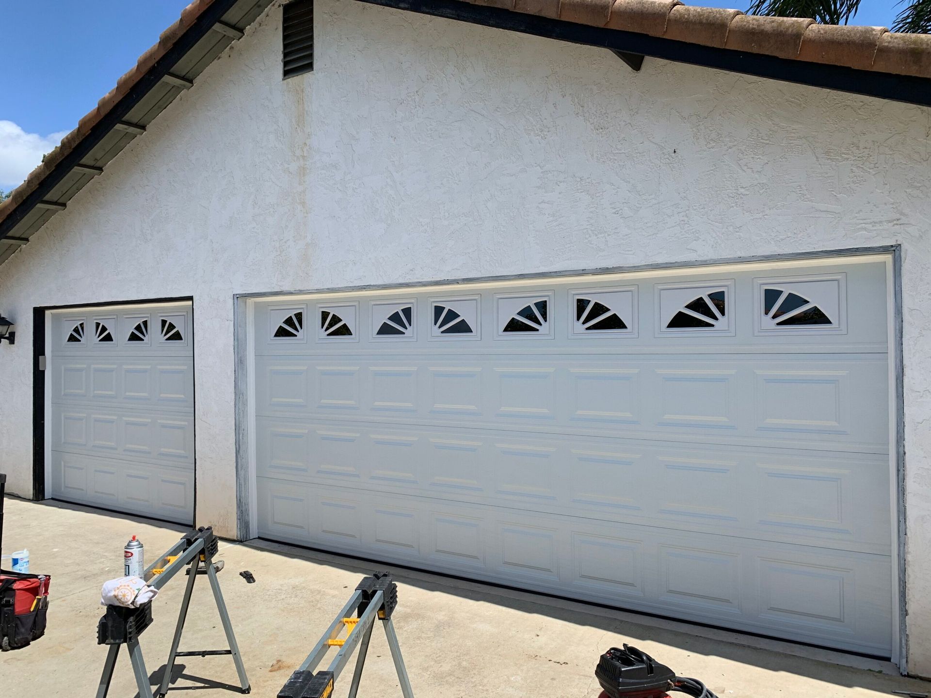 White two-car garage with decorative vents, viewed from the driveway with tools and ladders in front.