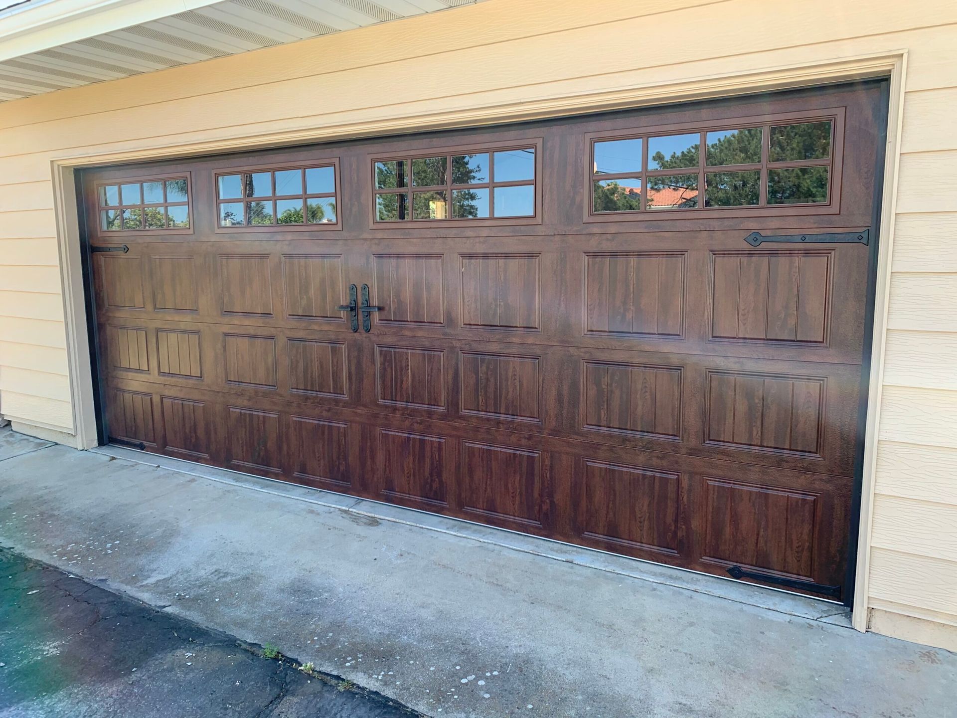 Brown garage door with four small windows, set in a beige house exterior.