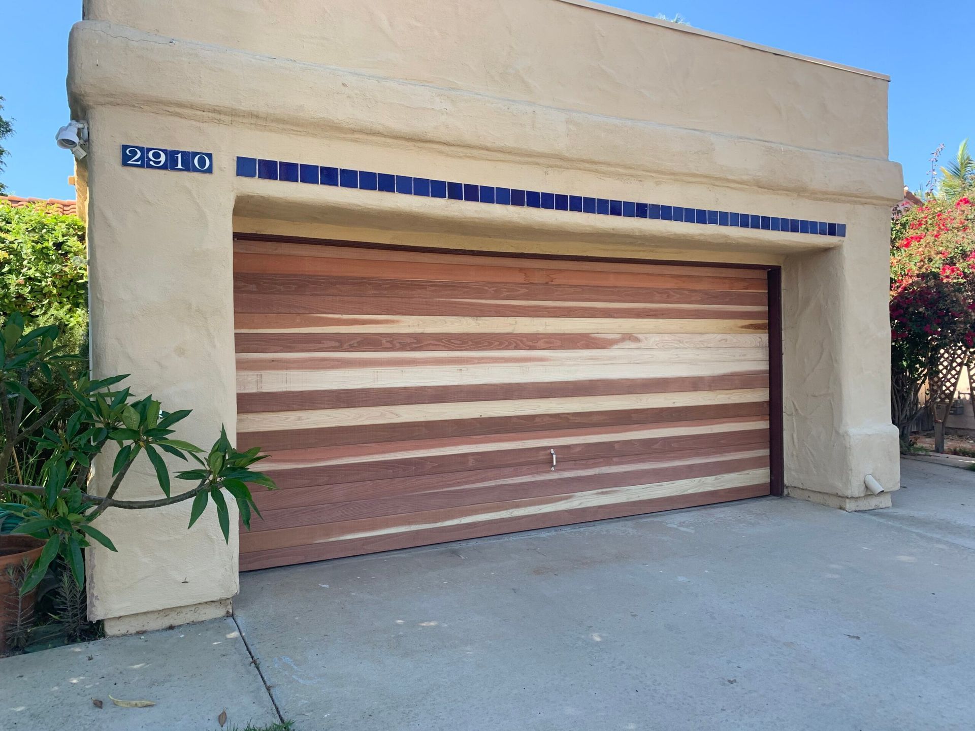 Beige garage with a wooden roll-up door and blue address plaque at the front of a house