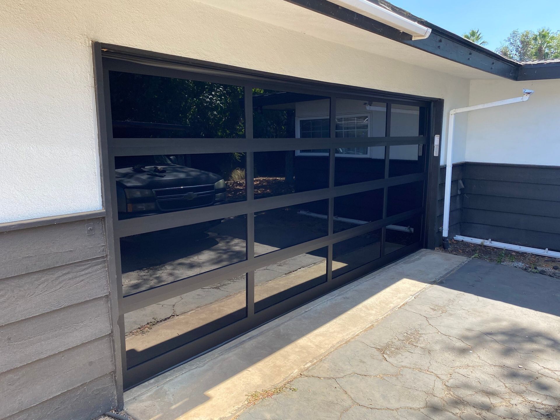Black-framed garage door with horizontal glass panels on a tan house exterior.
